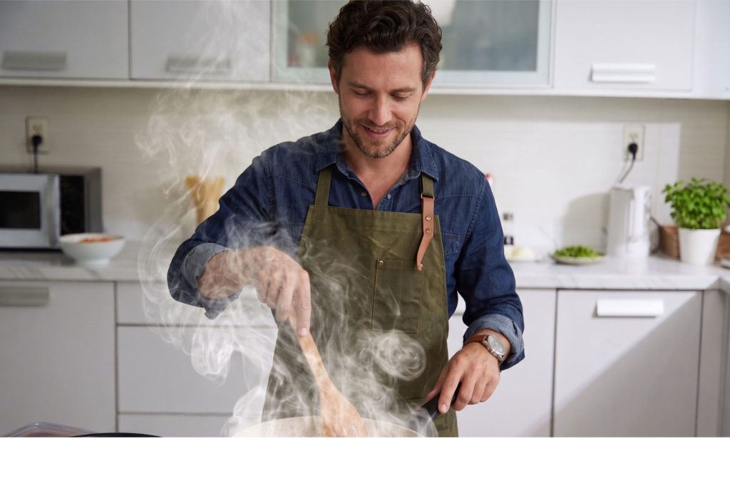 man die aan het koken is, er komt stoom van de pan af.